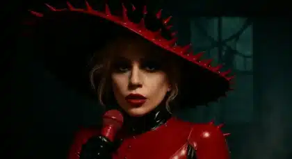 Lady Gaga wearing a red spiked outfit and hat, holding a red microphone in a moody, dark room